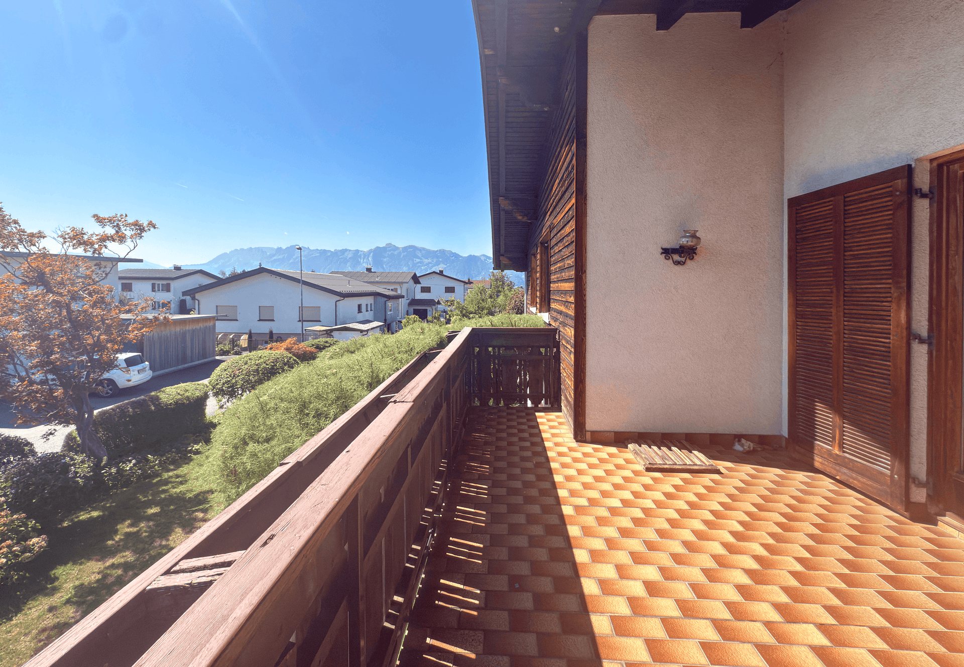 Sonniger Balkon mit traditionellem Holzgeländer und Panoramablick auf die Berge.