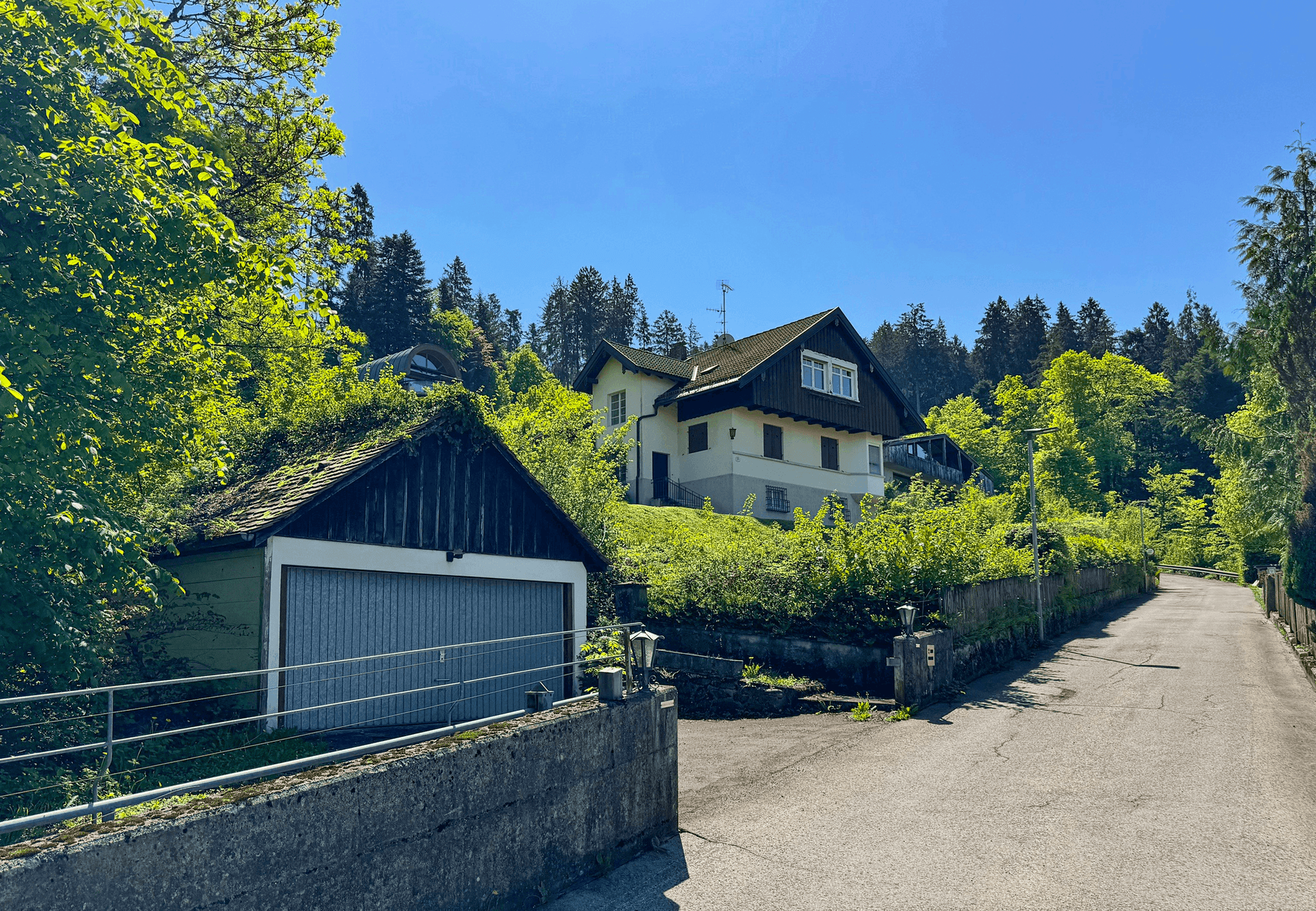 Haus und separate Garage von der Straße aus, eingebettet in grüne Umgebung und Bäume.