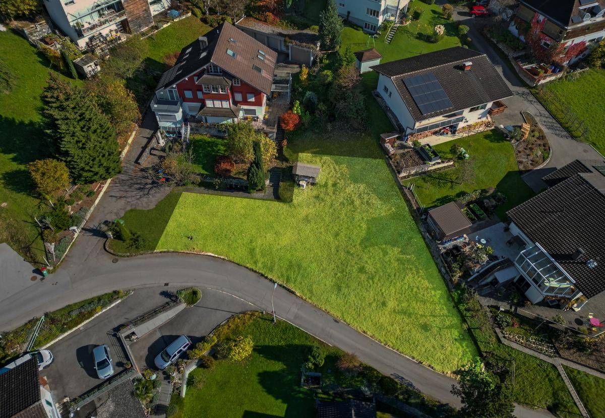 Luftaufnahme eines grün markierten Grundstücks, umgeben von Wohnhäusern und einer Zufahrtsstraße.