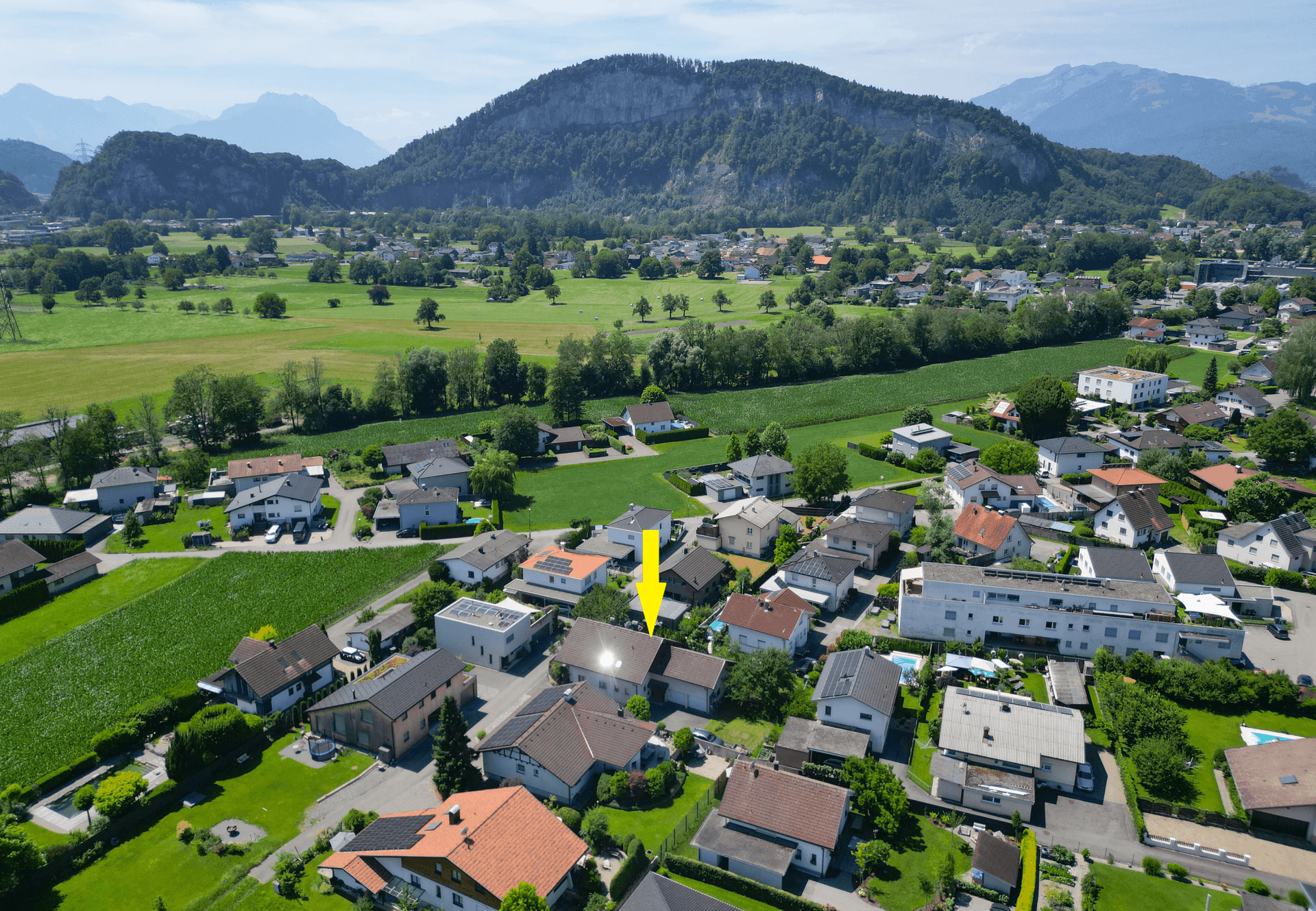 Panoramablick aus der Luft auf die Wohnsiedlung mit dem markierten Objekt und Bergkulisse.