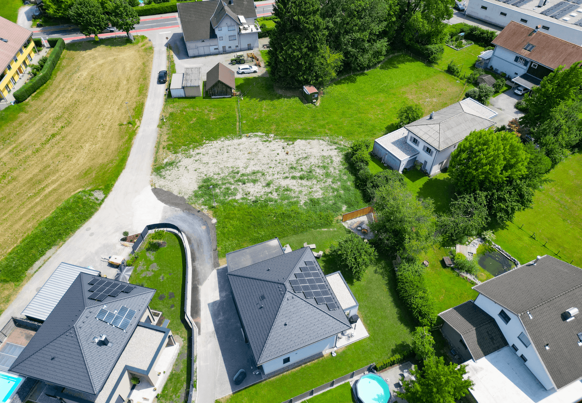 Vogelperspektive auf ein Baugrundstück, umgeben von Wohnhäusern, einige mit Garten und Pool.