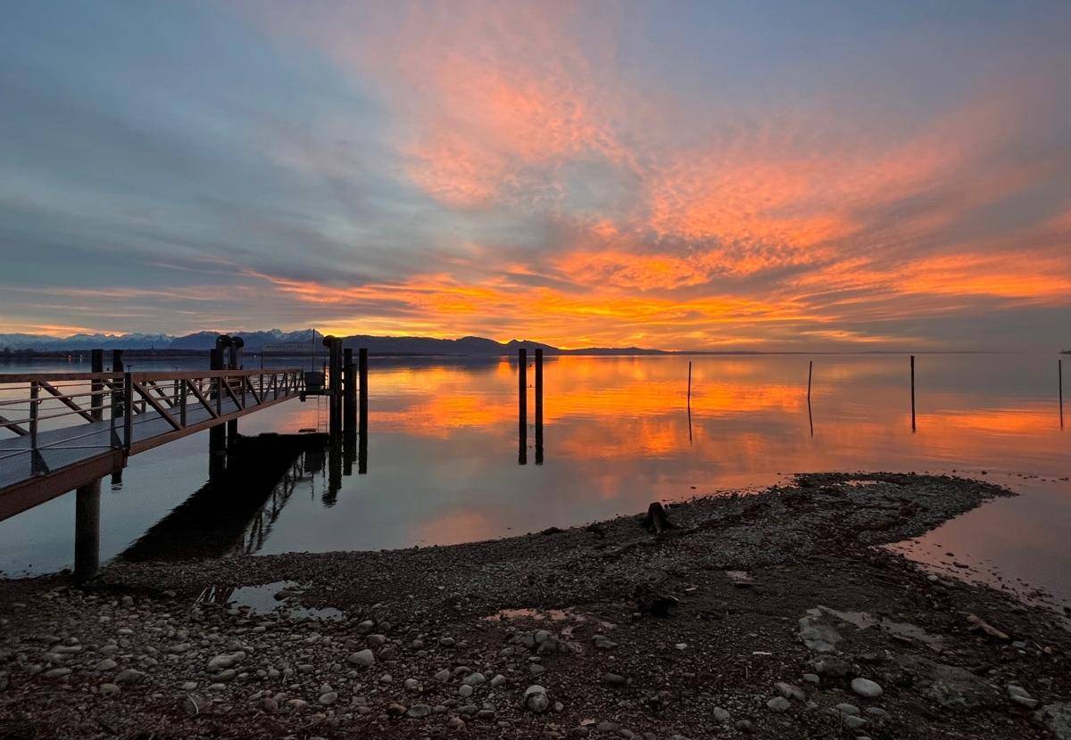 Spektakulärer Sonnenuntergang über dem See mit einem langen Steg und ruhigem Wasser.