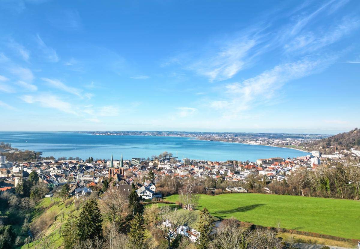 Weitläufige Luftaufnahme einer Stadt am Ufer des Bodensees unter klarem Himmel.