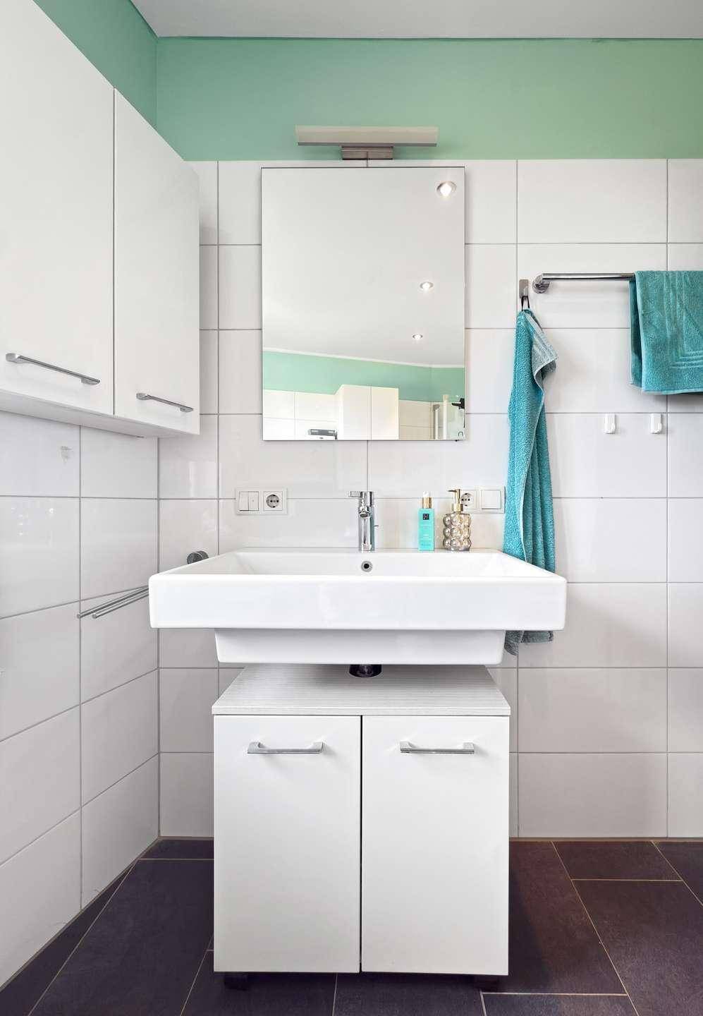 Badezimmer mit modernem Waschbecken, Spiegelschrank und weißen Wandfliesen.