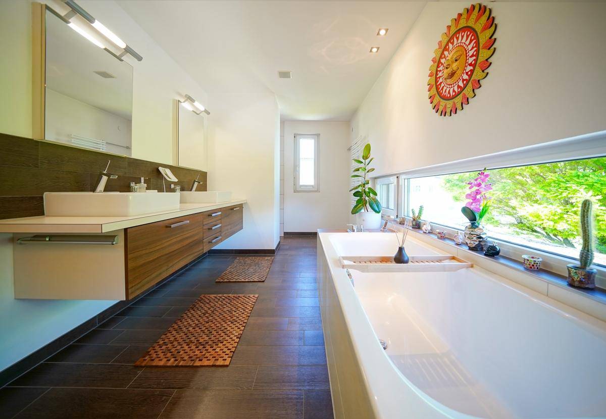 Langes Badezimmer mit Badewanne unter dem Fenster, Doppelwaschbecken und viel Tageslicht.