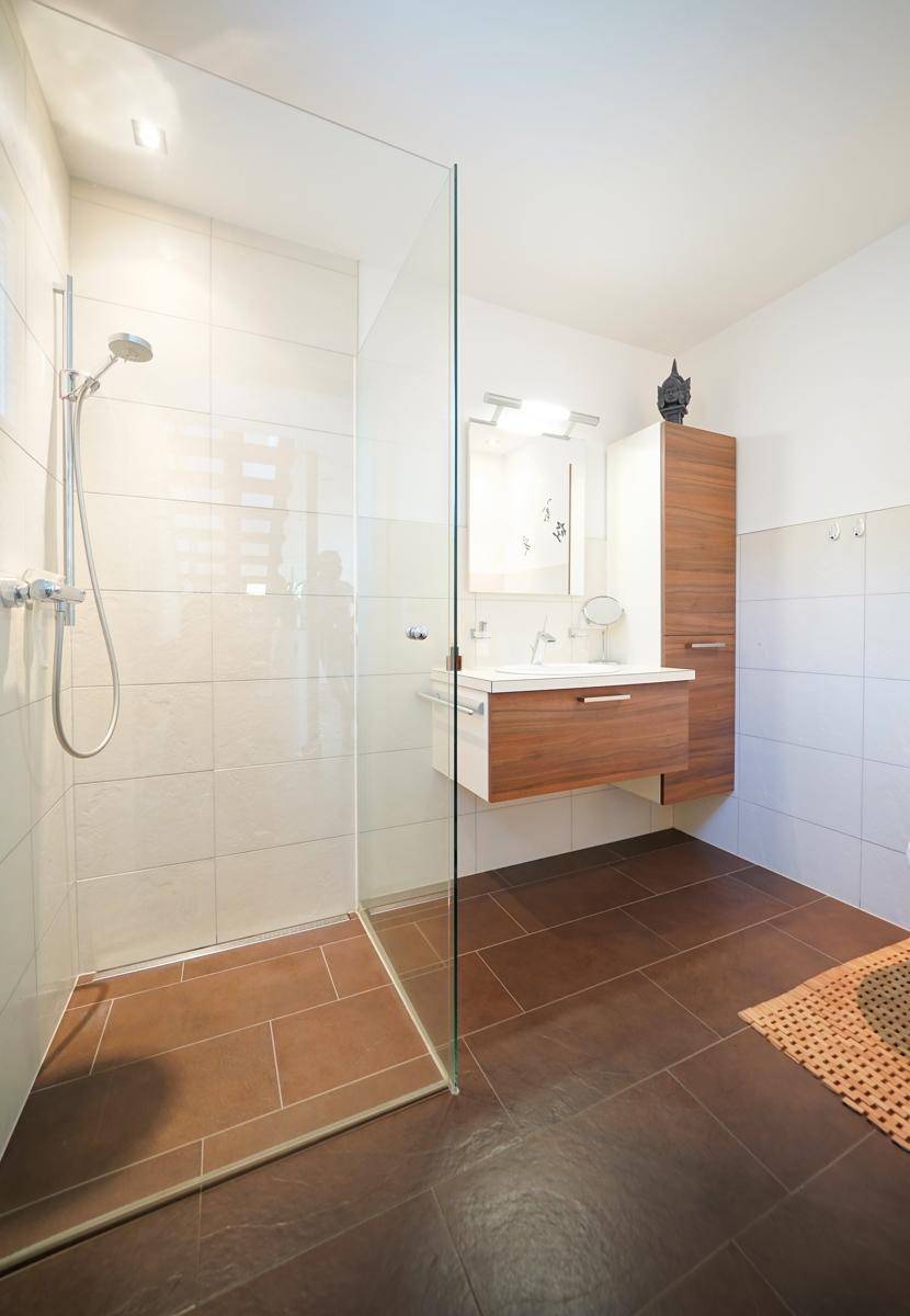 Modernes Badezimmer mit ebenerdiger Dusche, Waschtisch und weißen Fliesen.