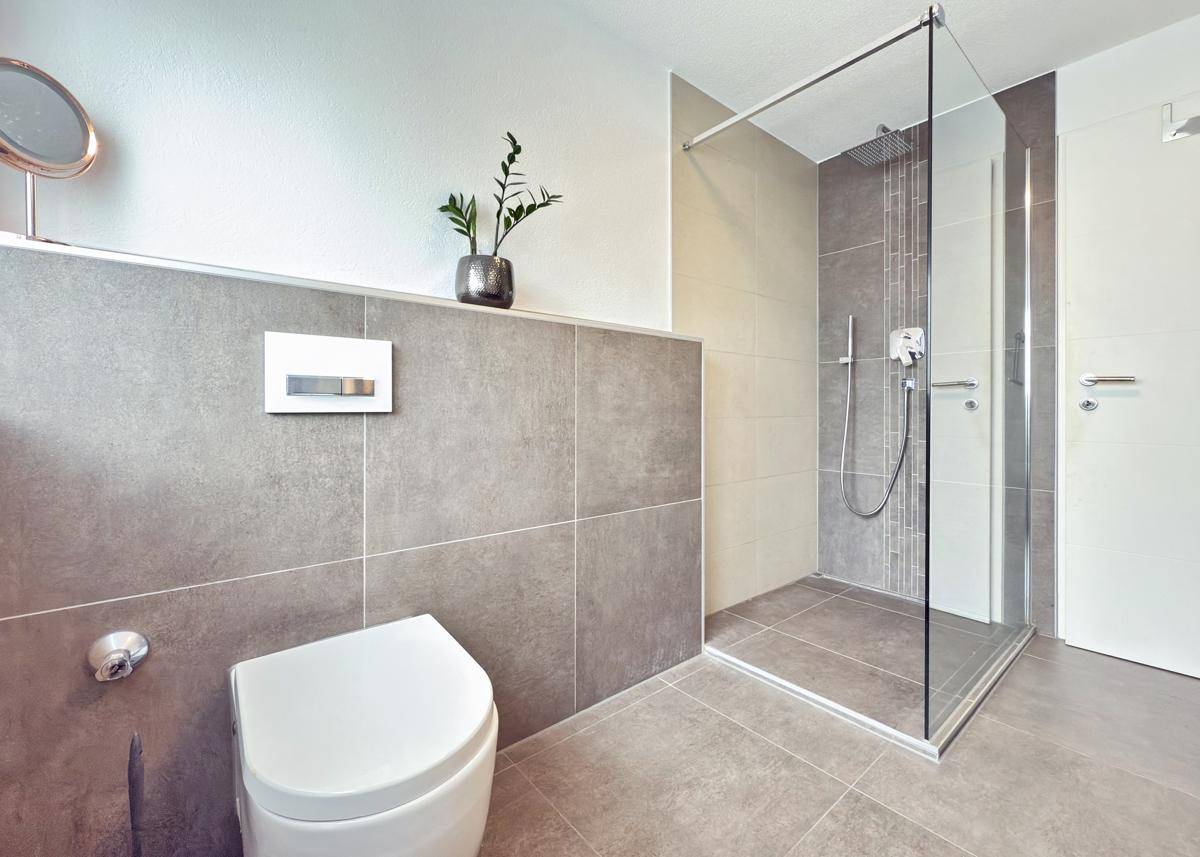 Modernes Badezimmer mit ebenerdiger Dusche, Wand-WC und grauen Fliesen.