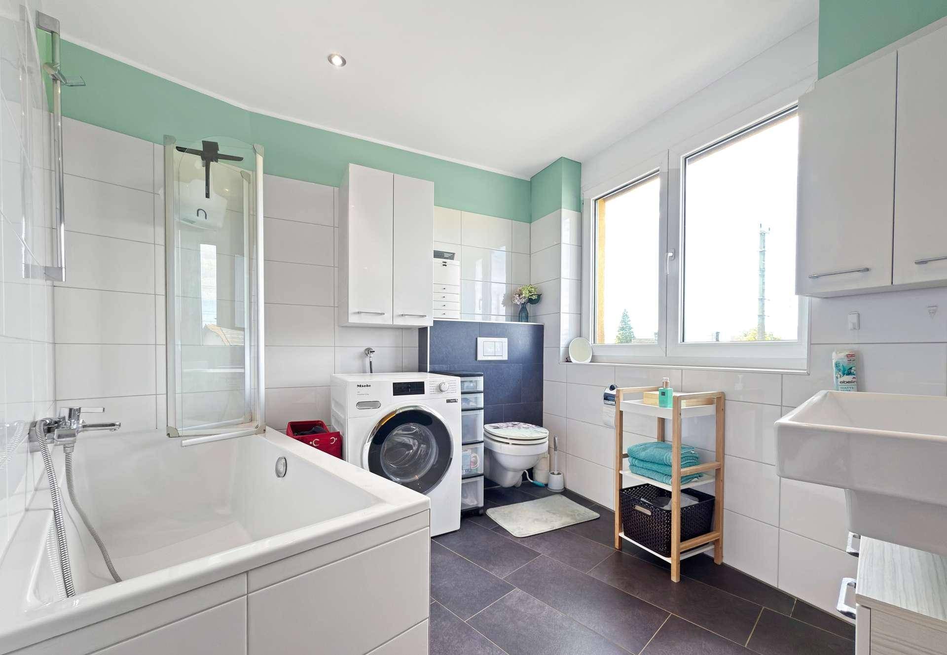 Geräumiges Badezimmer mit Badewanne, Waschmaschine, WC und Fenster.