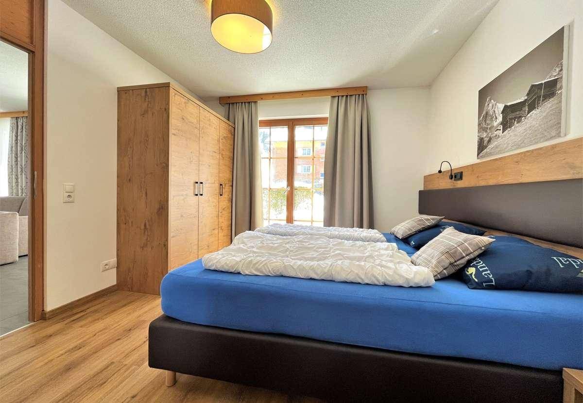 Komfortables Schlafzimmer mit Holzbett, Kleiderschrank und Zugang zum Balkon.