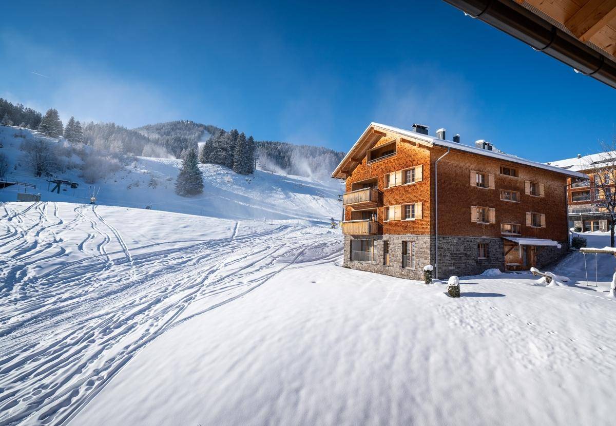 Chalet in verschneiter Landschaft mit Skipisten im Hintergrund, ideal für Wintersportler.
