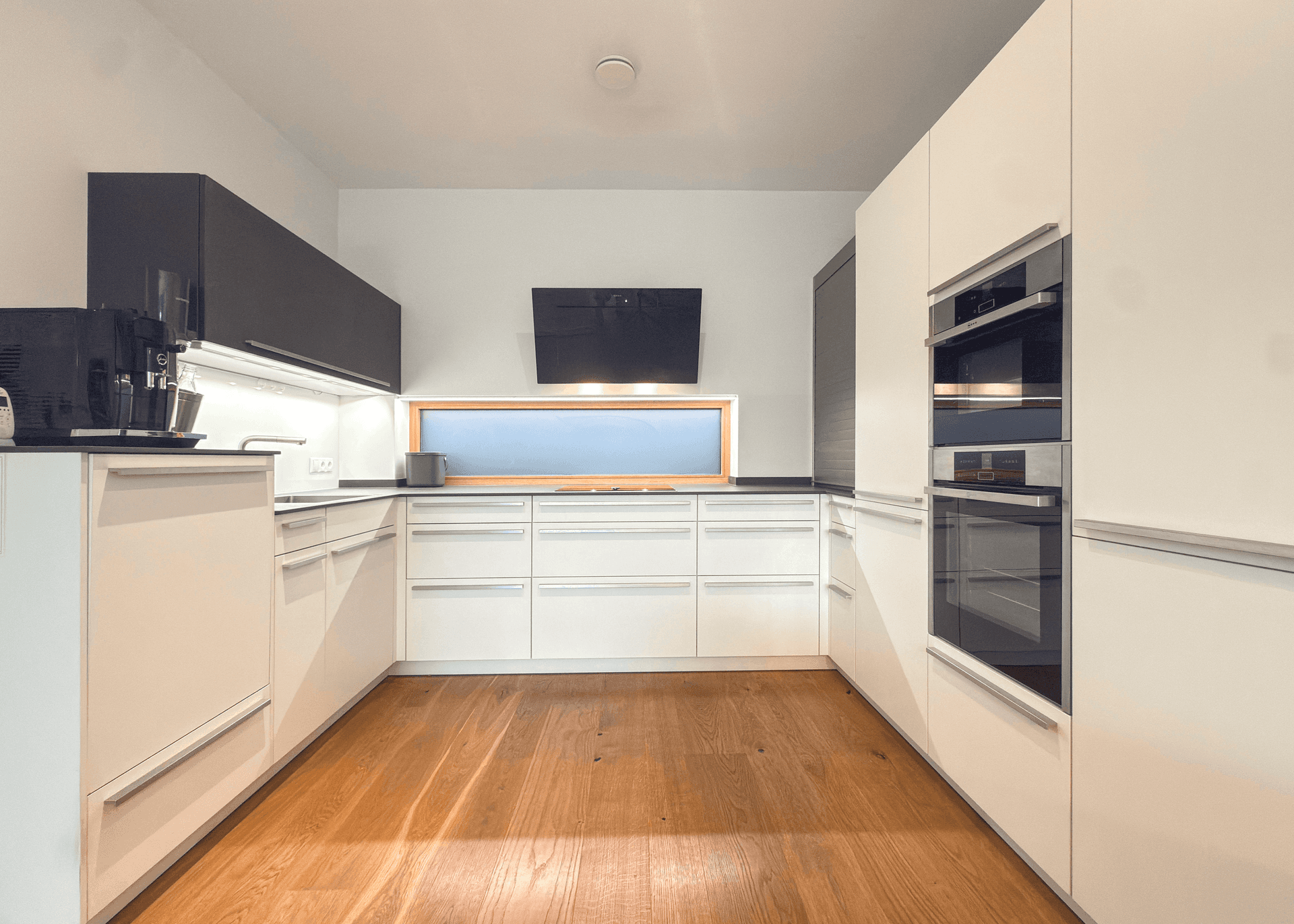 Helle, moderne Küche mit weißen Hochglanzfronten, integrierten Geräten und Holzfußboden.