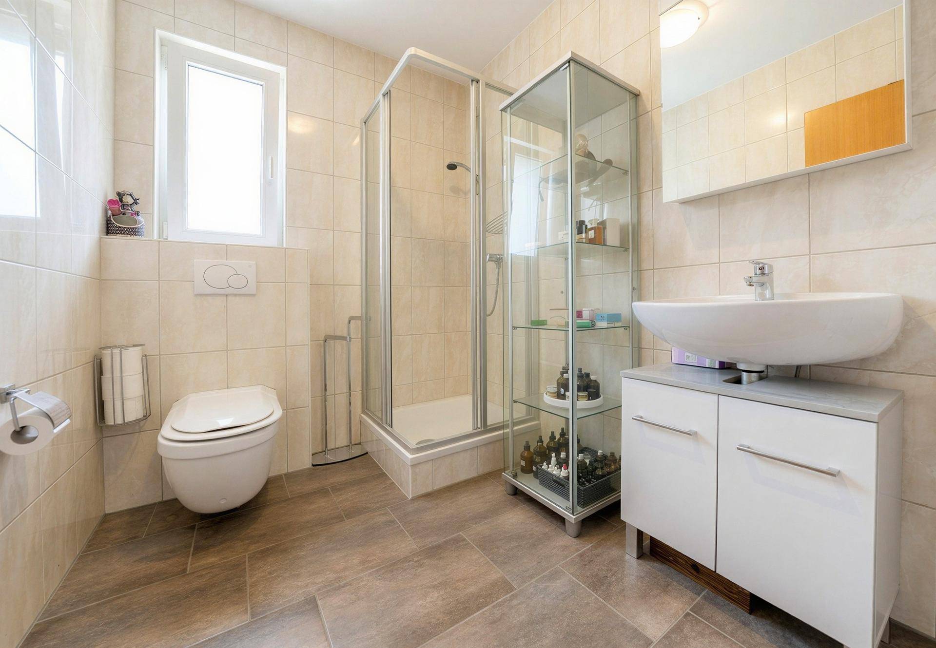 Funktionales Badezimmer mit WC, Duschkabine, Waschtisch und Fenster.