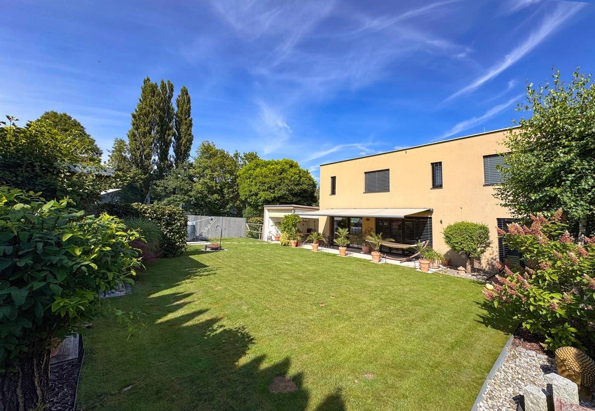 Großer, gepflegter Garten mit Rasenfläche und moderner Hausfassade im Hintergrund.
