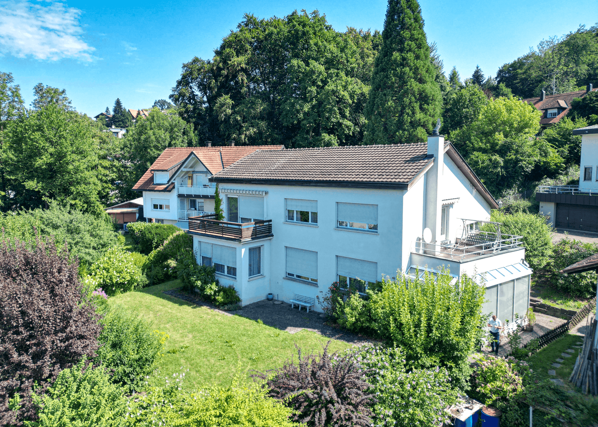 Luftaufnahme eines Hauses mit gepflegtem Garten und Terrasse in einer grünen Umgebung.
