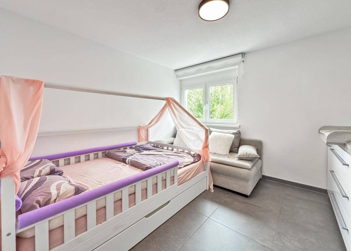 Kinderzimmer mit Himmelbett, Sofa und Fenster mit Blick ins Grüne.