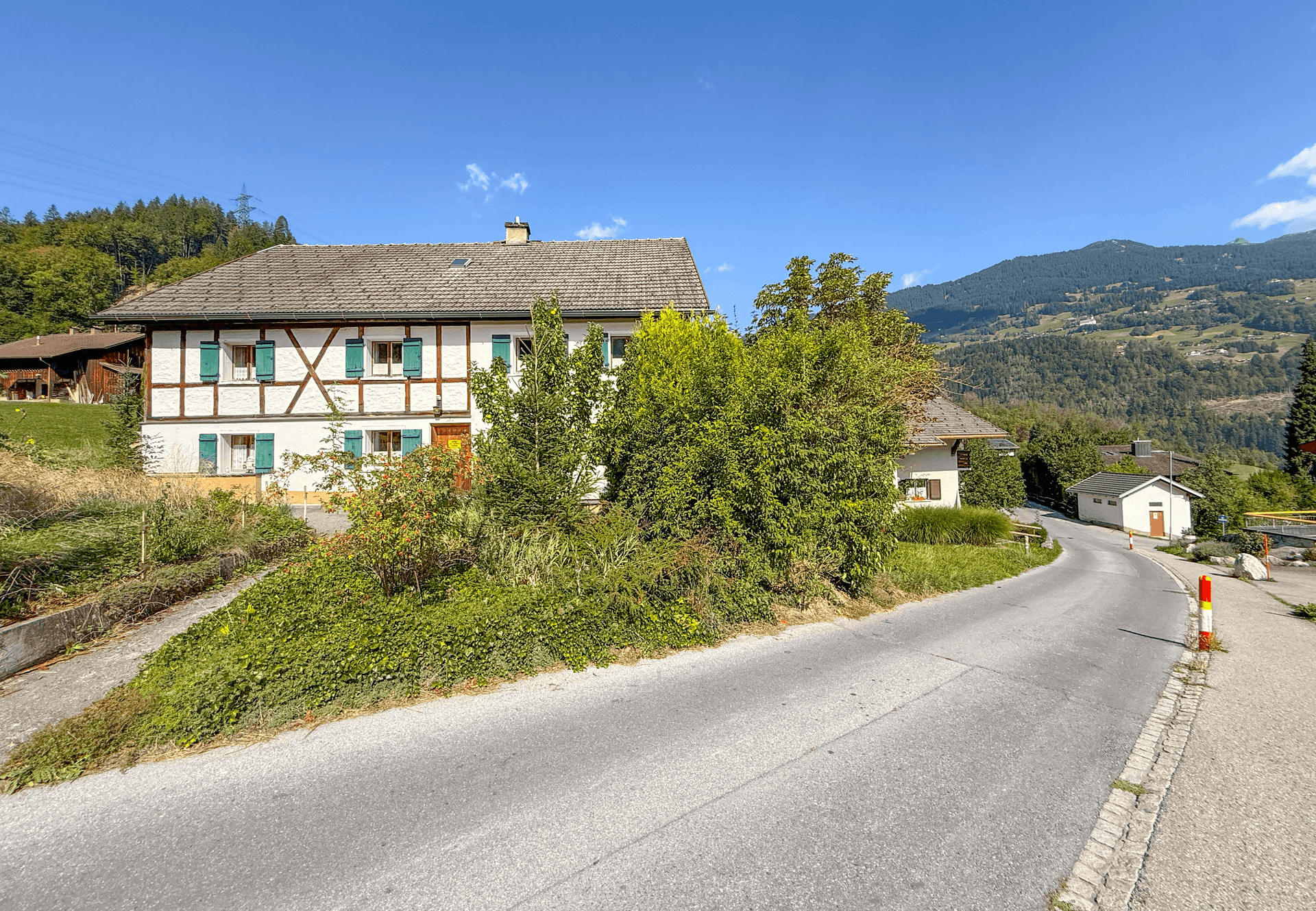 Vorderansicht des traditionellen Hauses mit weißer Fassade, grünen Fensterläden und einer Zufahrtsstraße.