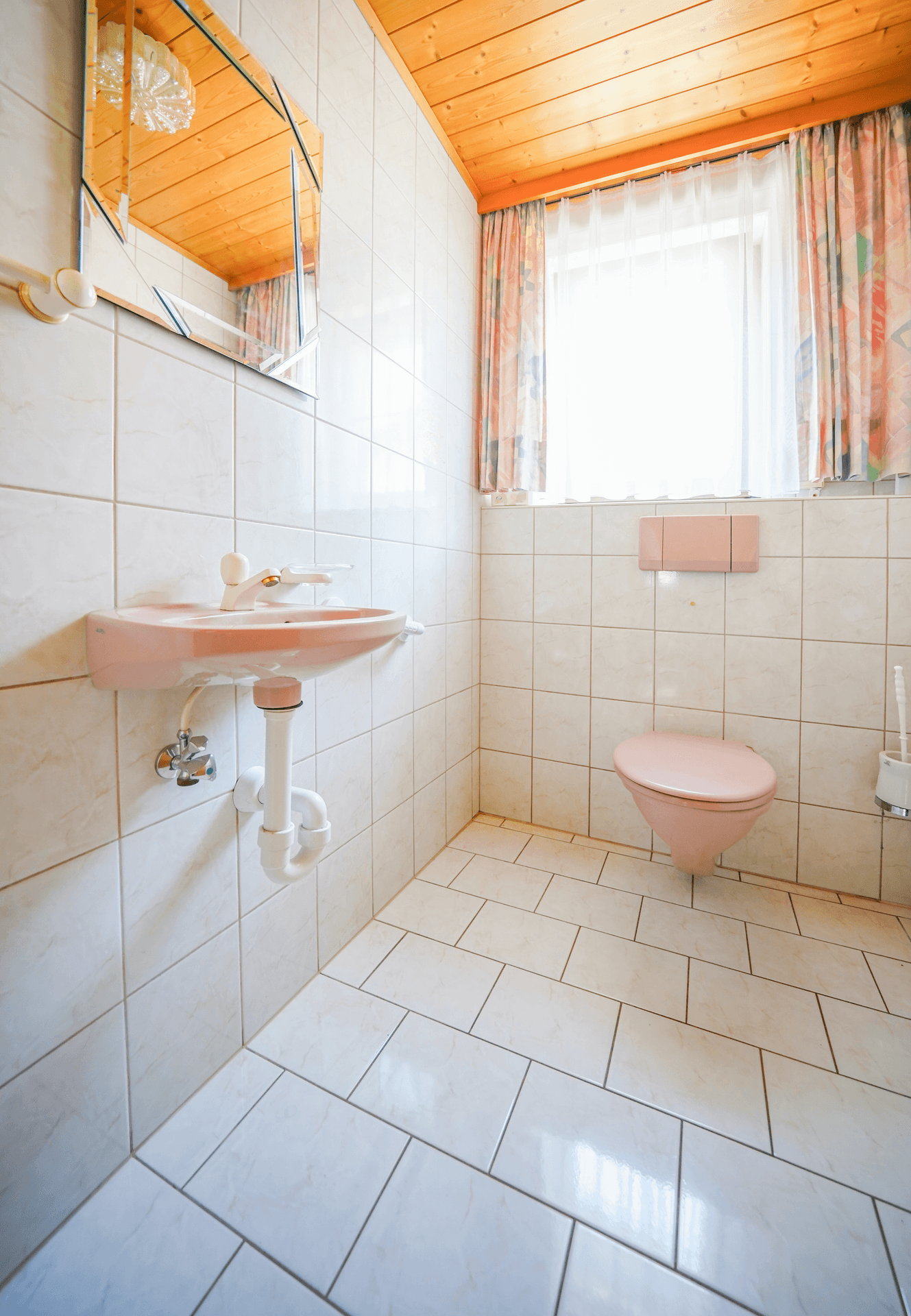 Kleines Gäste-WC mit rosa Sanitärobjekten, Fliesenwänden und Holzdecke.