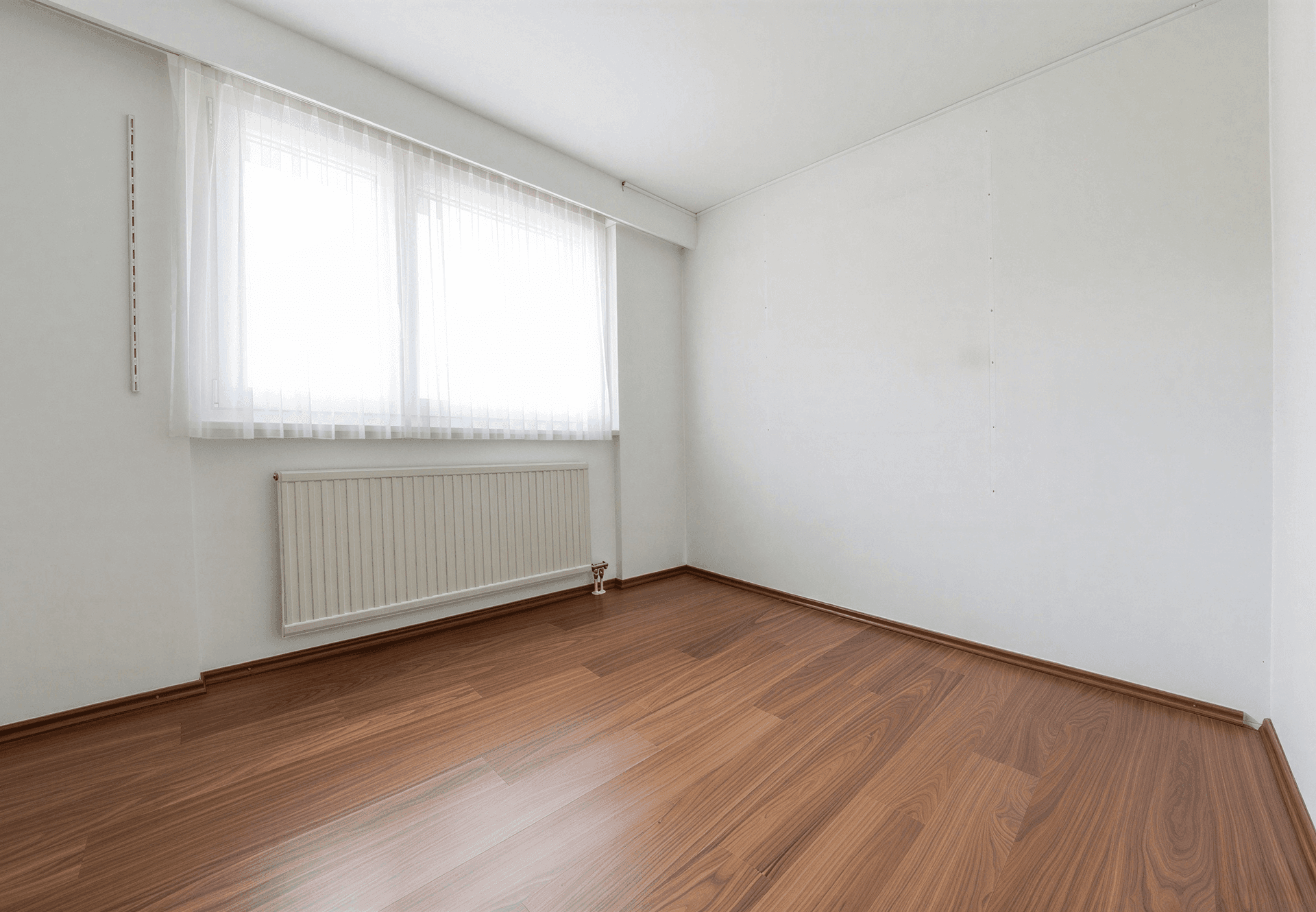Leeres Zimmer mit Holzboden und großem Fenster, bereit zur individuellen Gestaltung.