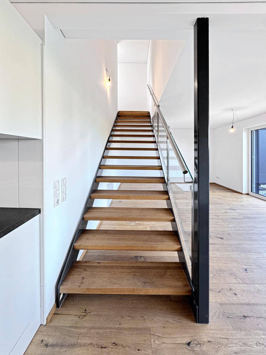 Moderne Holztreppe mit Glasgeländer, die die verschiedenen Ebenen verbindet.