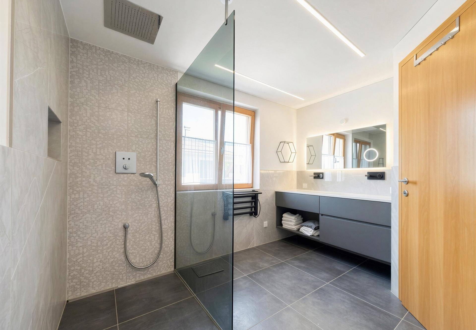 Modernes Badezimmer mit großer begehbarer Dusche, grauen Fliesen und Fenster.