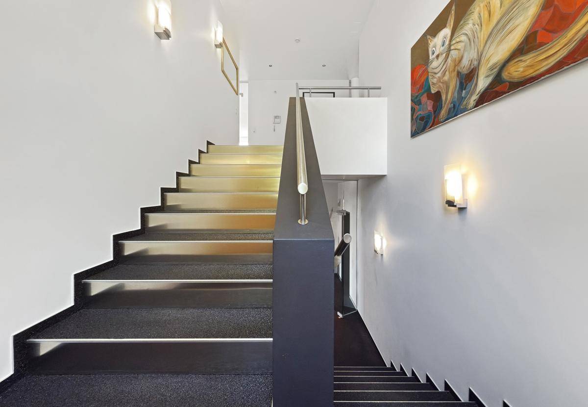 Moderne Treppe mit Teppichstufen, Edelstahlgeländer und Kunstwerken an der Wand.
