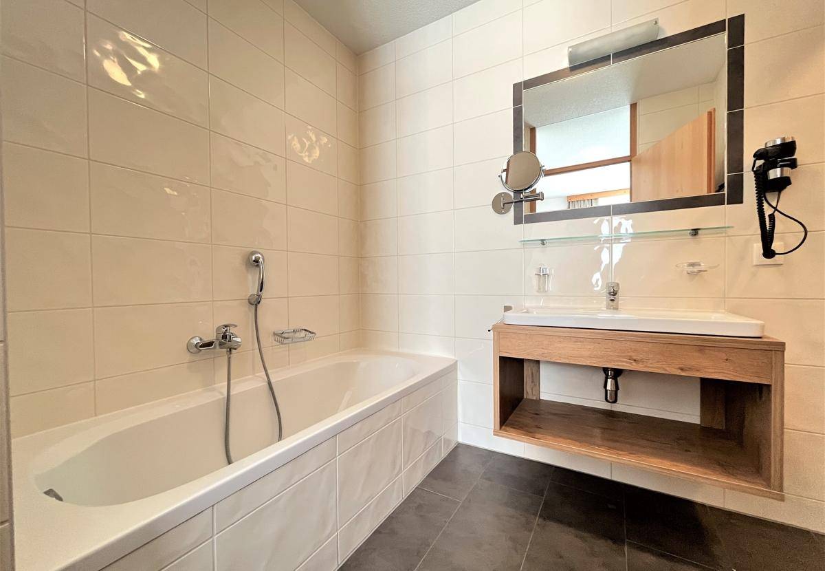 Helles Badezimmer mit Badewanne, Einzelwaschbecken und großem Spiegel, modern gefliest.