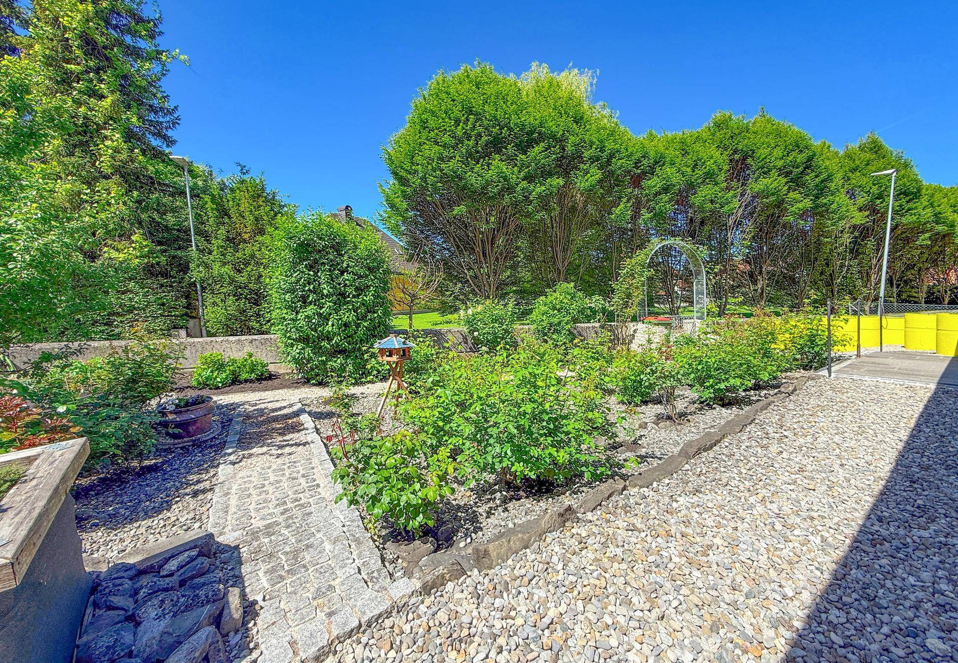Weitläufiger Gartenbereich mit Kieswegen, hohen Hecken und alten Bäumen.