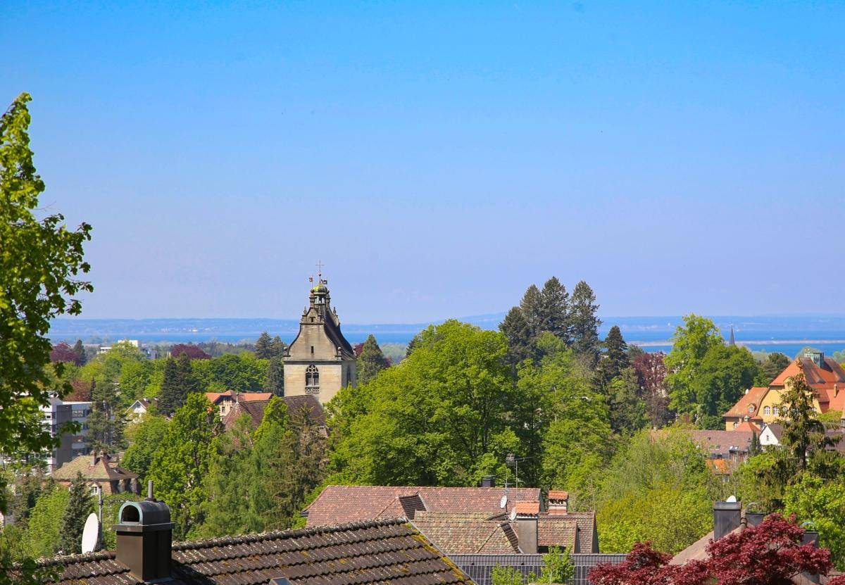 Weitblick über Dächer und einen Kirchturm auf die Stadt und den Bodensee.
