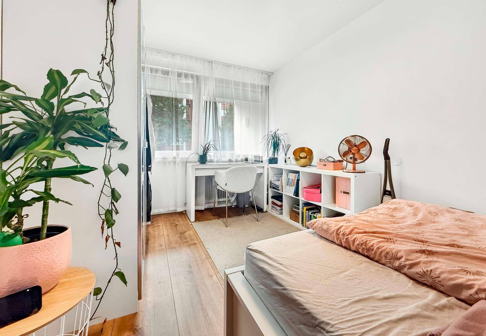 Schlafzimmer mit Schreibtisch am Fenster, Holzboden und viel Tageslicht.