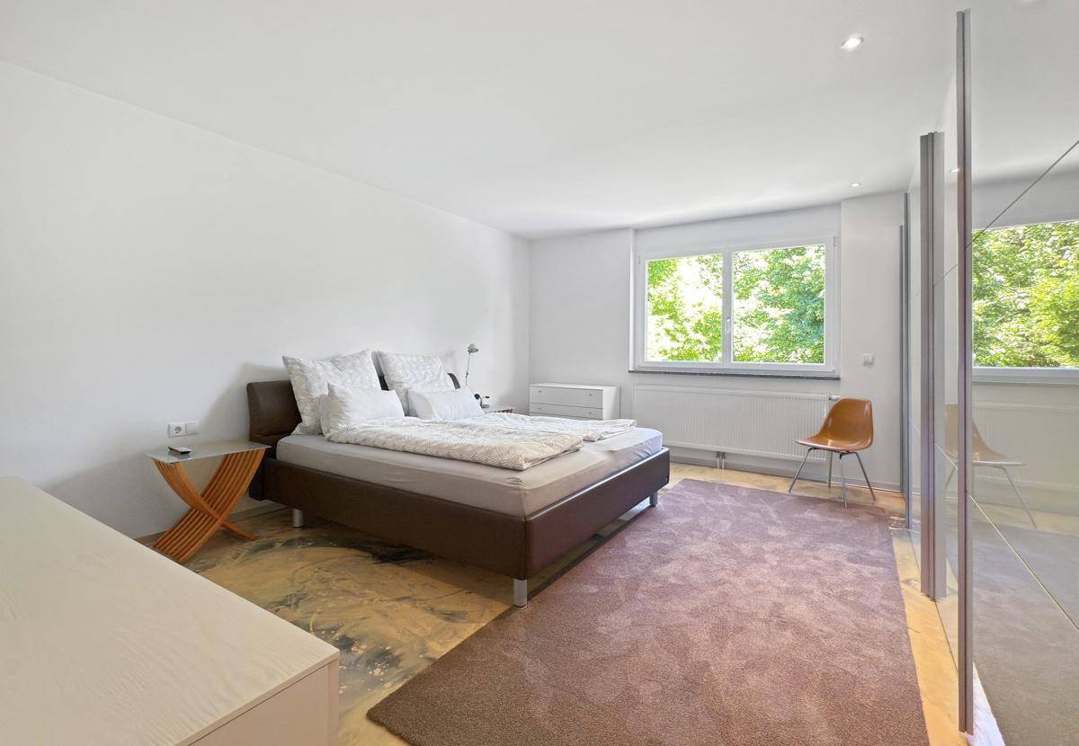Helles Schlafzimmer mit Doppelbett, Teppichboden und großen Fenstern mit Blick ins Grüne.