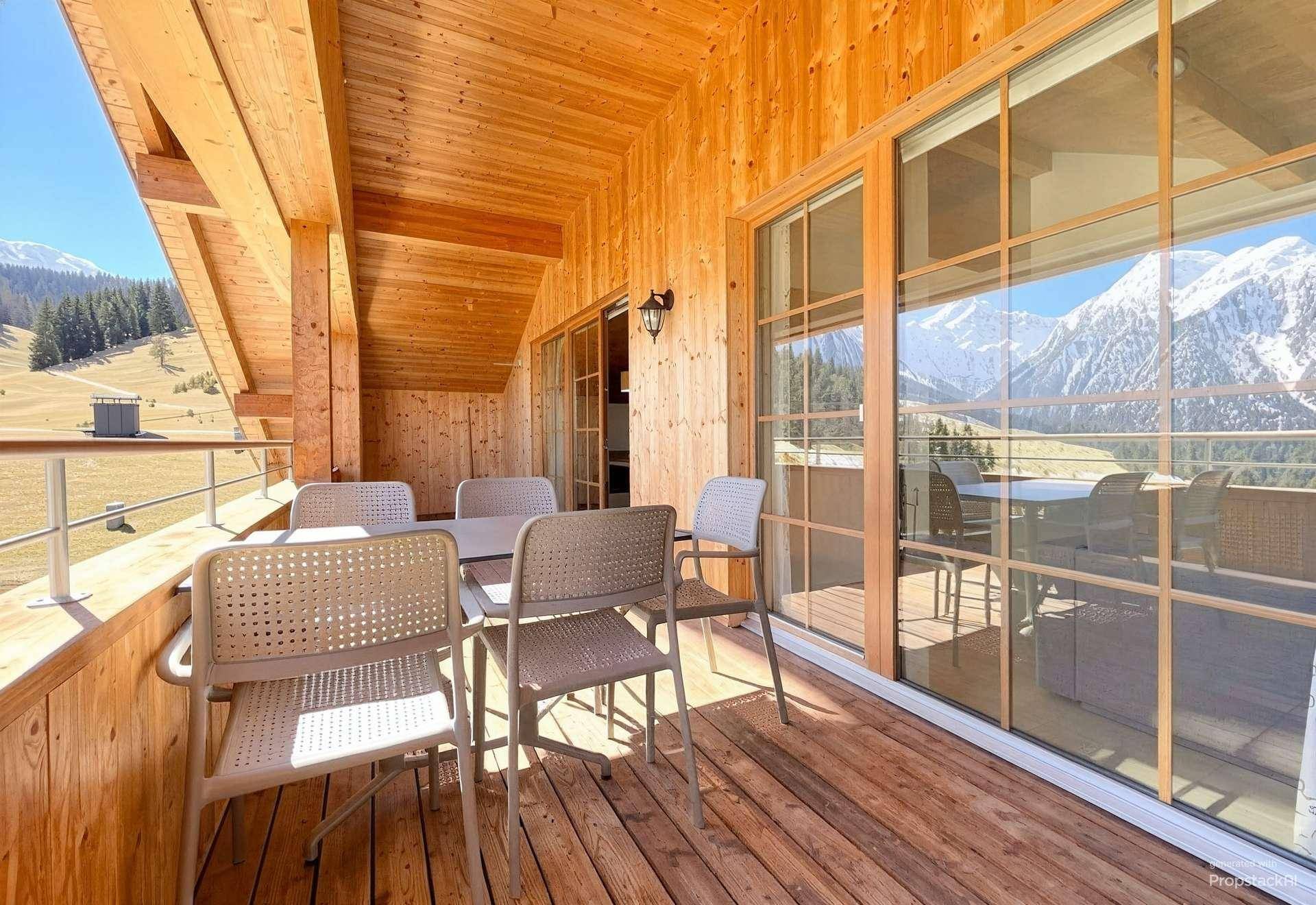 Geräumiger Holzbalkon mit Sitzgelegenheiten und weitem Blick über grüne Hügel und Berge.