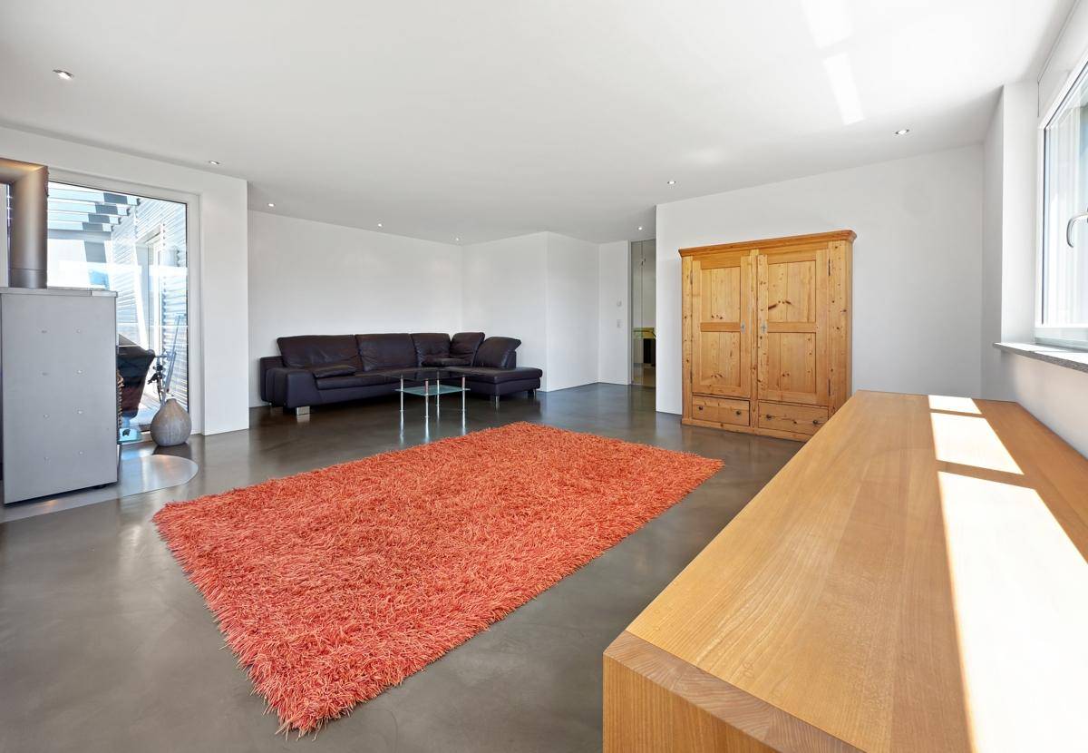 Geräumiges Wohnzimmer mit hellem Holzboden, Kaminofen und einem großen Fenster.