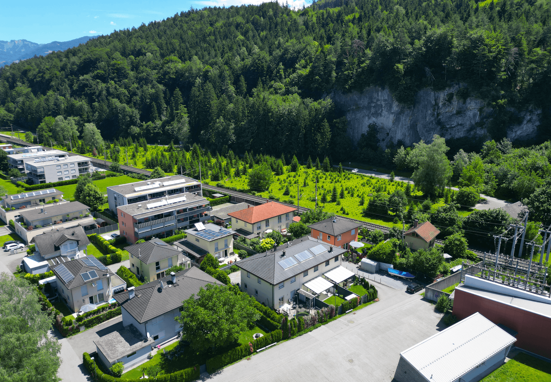 Luftaufnahme der Wohngegend mit Waldrand, Bahngleisen und Bergkulisse, bietet viel Natur.