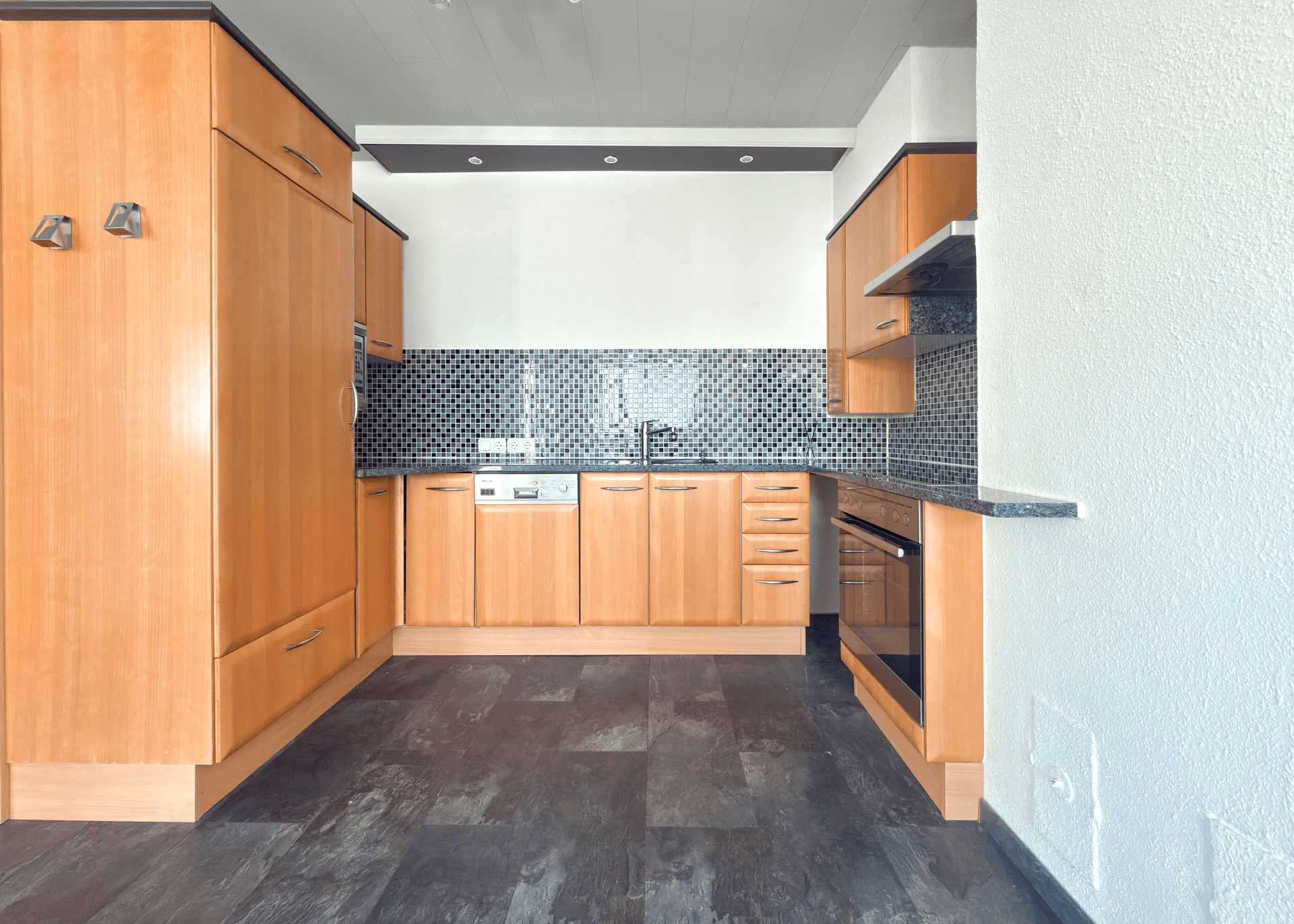 Funktionale Küche mit Holzschränken, dunklem Mosaikfliesenspiegel und Einbaugeräten.