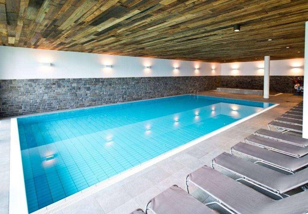 Großes Hallenbad mit Liegestühlen und rustikaler Holzdecke.