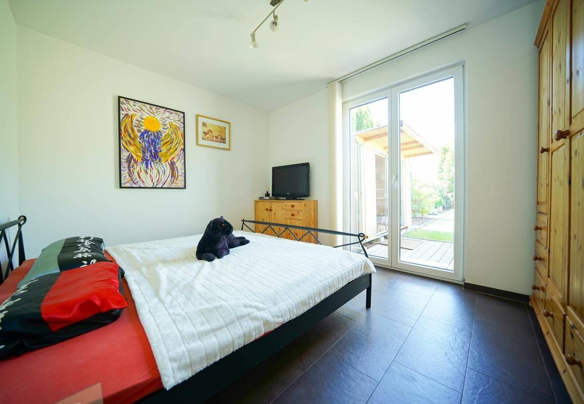 Helles Schlafzimmer mit Doppelbett, Holzkleiderschrank und Zugang zum Garten.