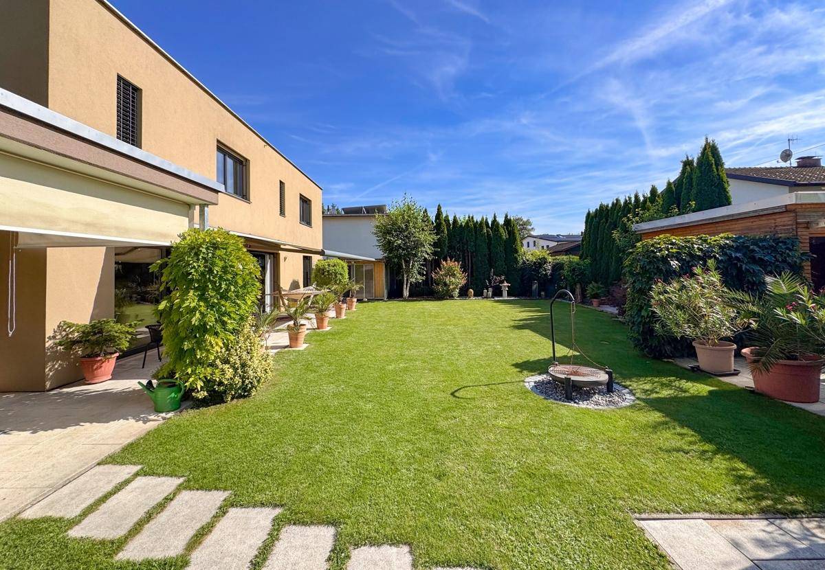 Grüner Garten mit Rasenfläche, Trittsteinen und einer Feuerstelle im Freien.