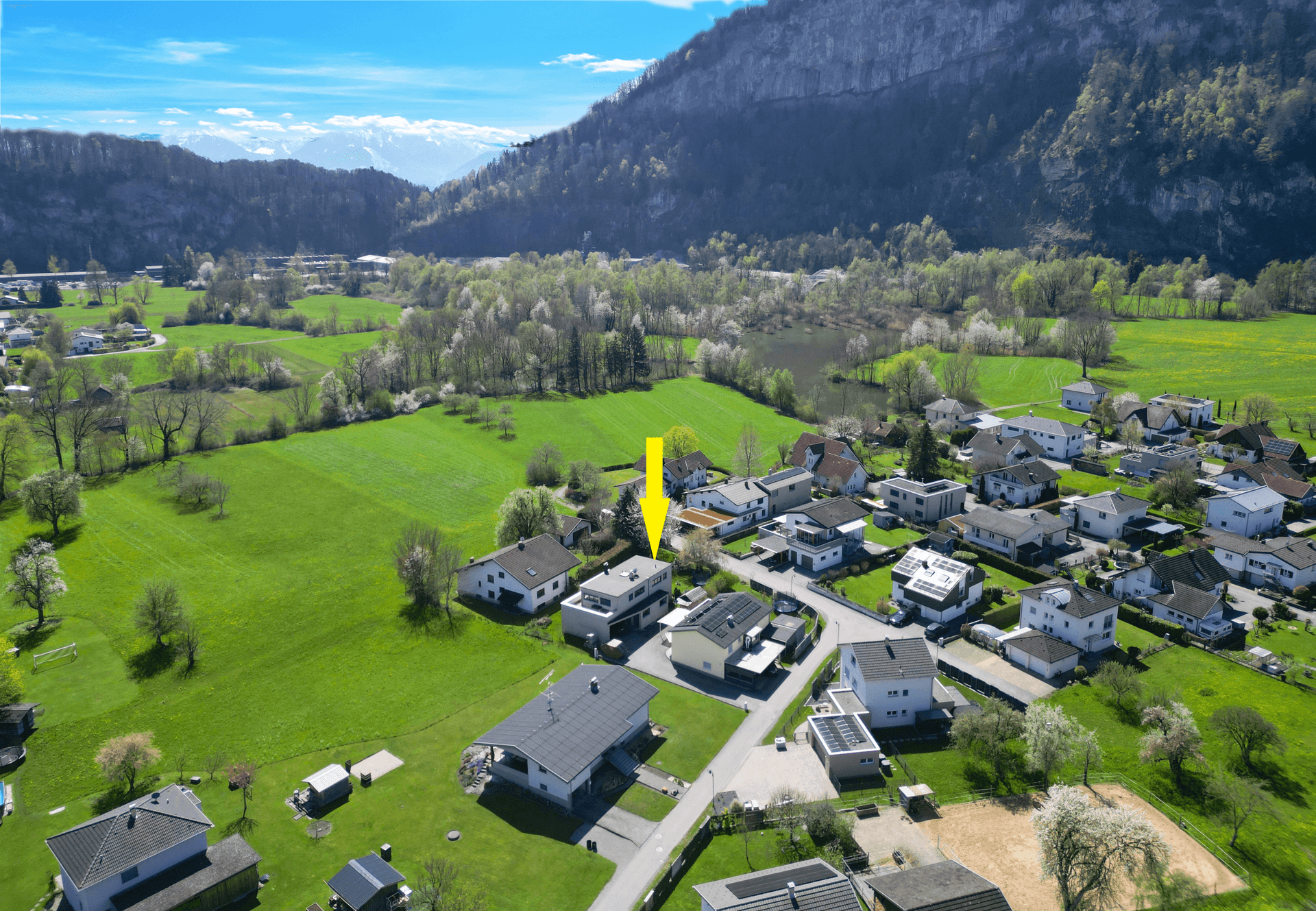 Weitläufige Luftaufnahme der Siedlung mit Bergen und einem Fluss oder See im Hintergrund.