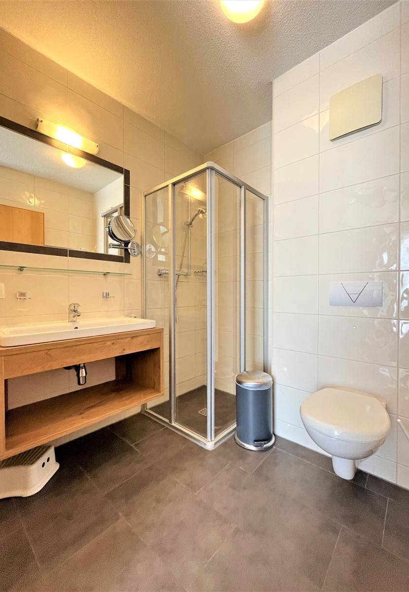 Modernes Badezimmer mit Duschkabine, Einzelwaschbecken und Wand-WC, hell gefliest.
