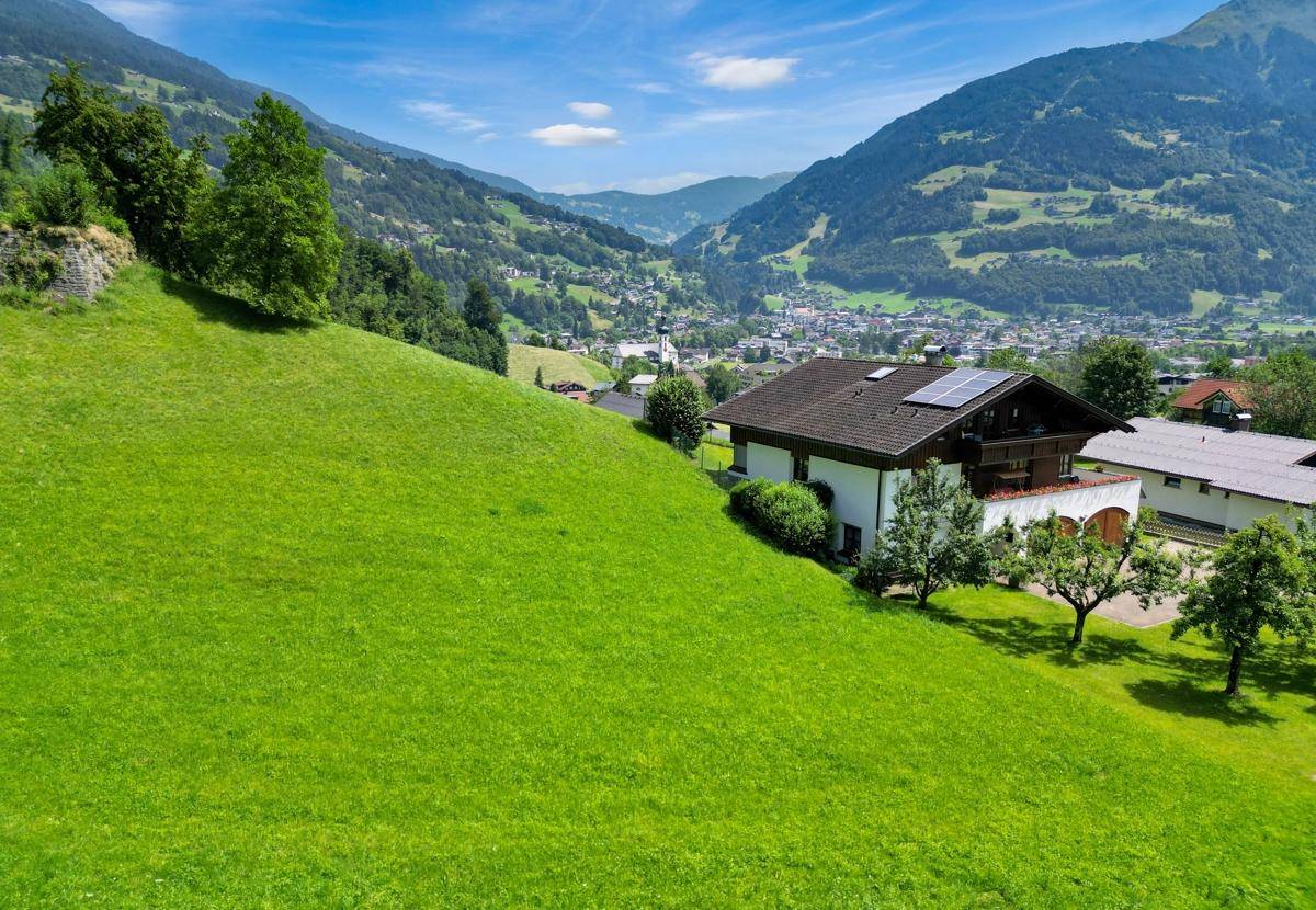 Haus auf einem grünen Hang mit Photovoltaikanlage und Blick auf ein Tal und eine Ortschaft.
