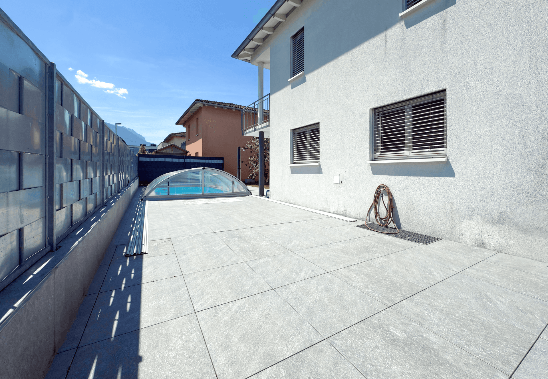 Geräumige geflieste Terrasse neben dem Haus mit Blick auf den Poolbereich.