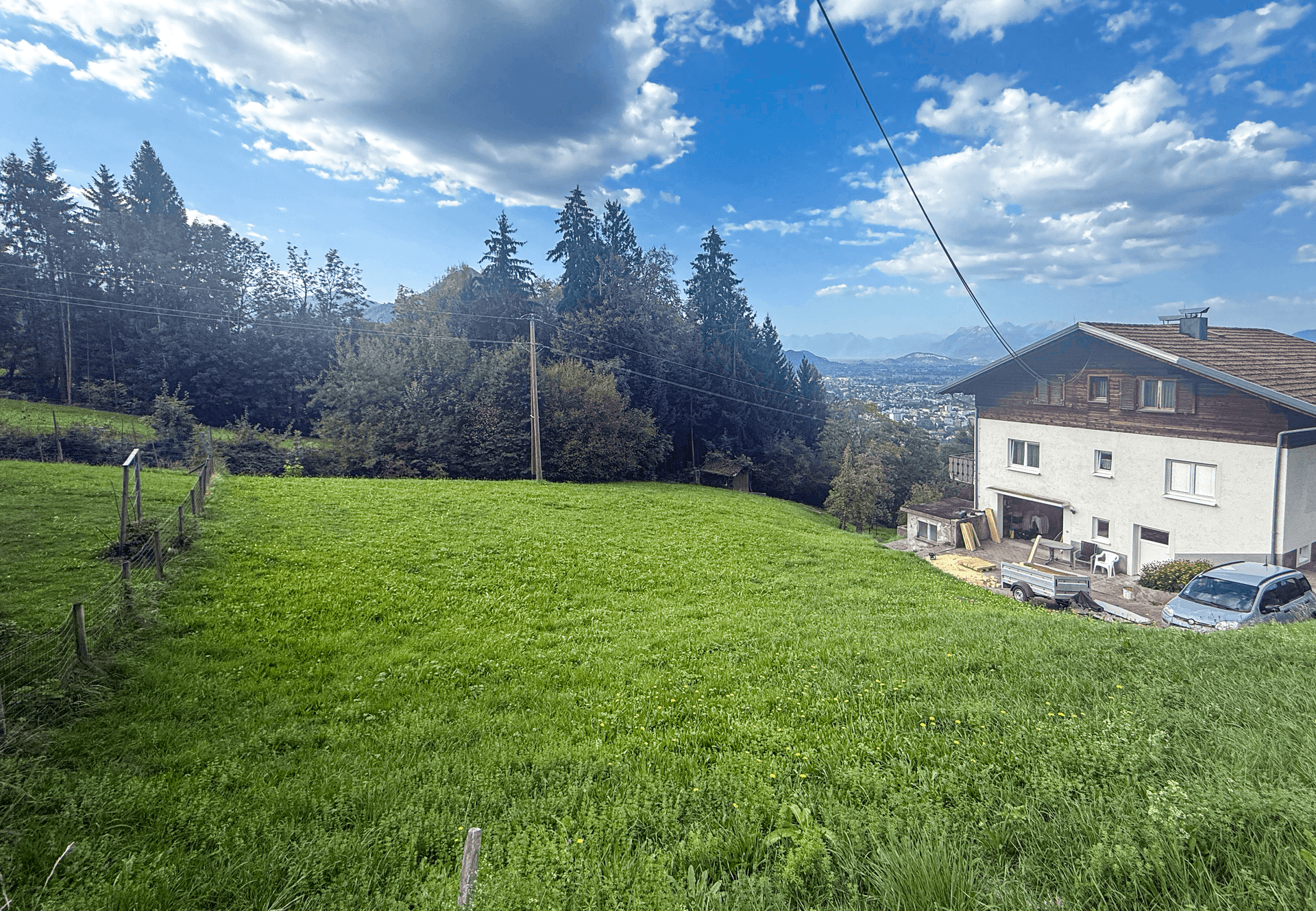 Weitläufiges grünes Feld neben einem Wohnhaus mit Blick auf die Stadt und Berge in der Ferne.