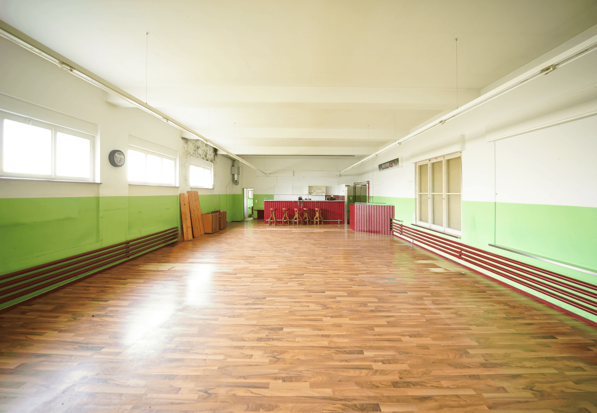 Großer offener Raum mit Laminatboden, grün-weißen Wänden und einem Barbereich im Hintergrund.