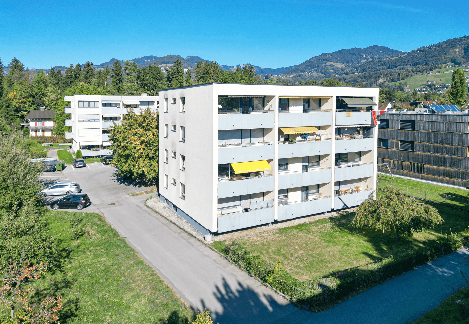 Mehrfamilienhaus in grüner Umgebung mit Balkonen und Blick auf die Berge.