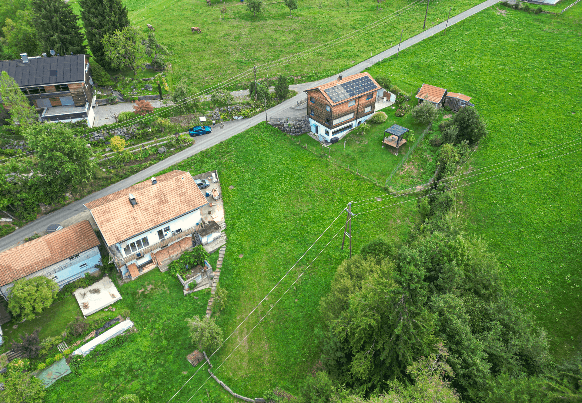 Vogelperspektive auf Wohnhäuser, eine Straße und weitläufige grüne Felder in ländlicher Umgebung.