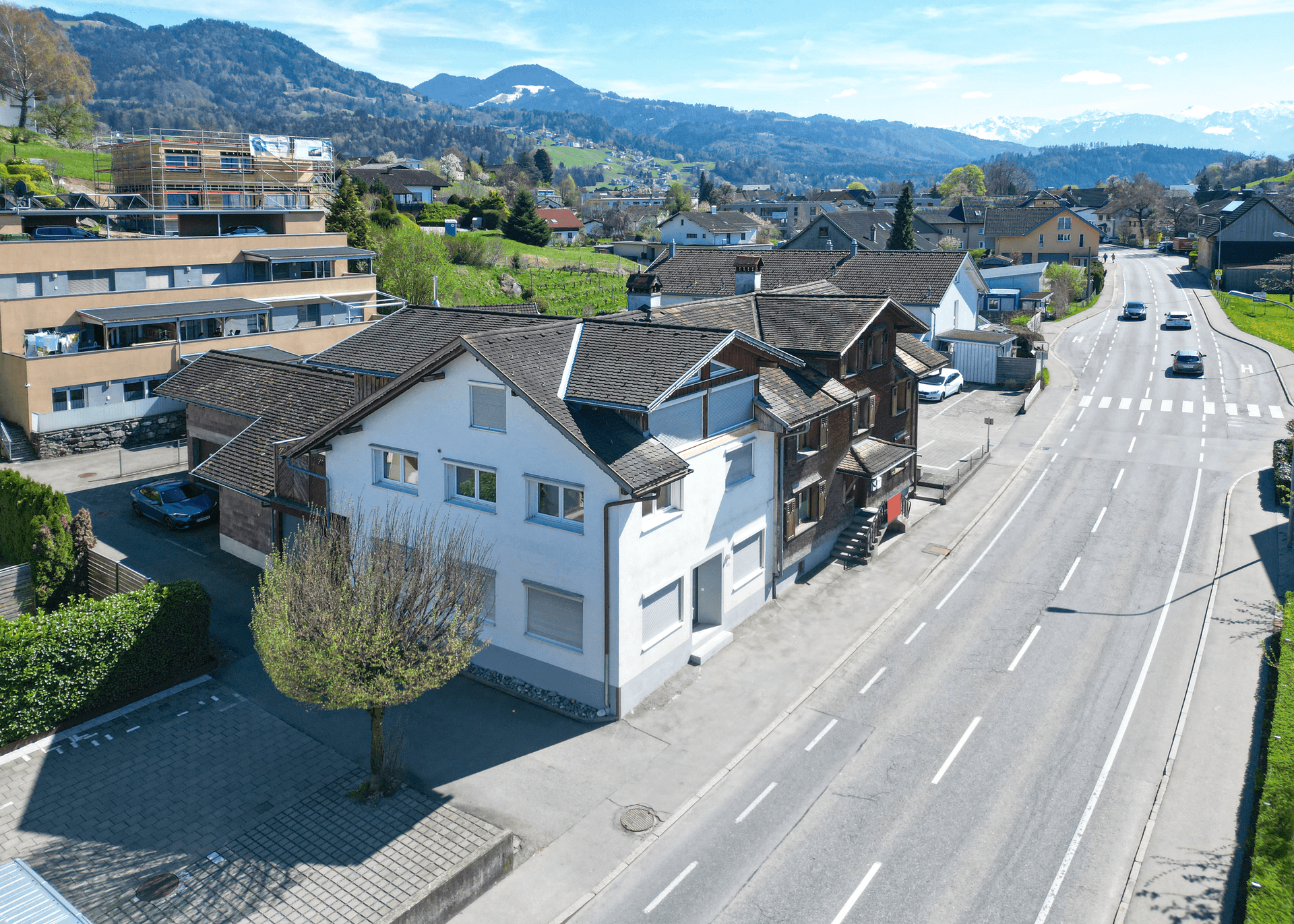 Luftaufnahme eines Wohngebäudes an einer Straße mit bergiger Landschaft im Hintergrund.