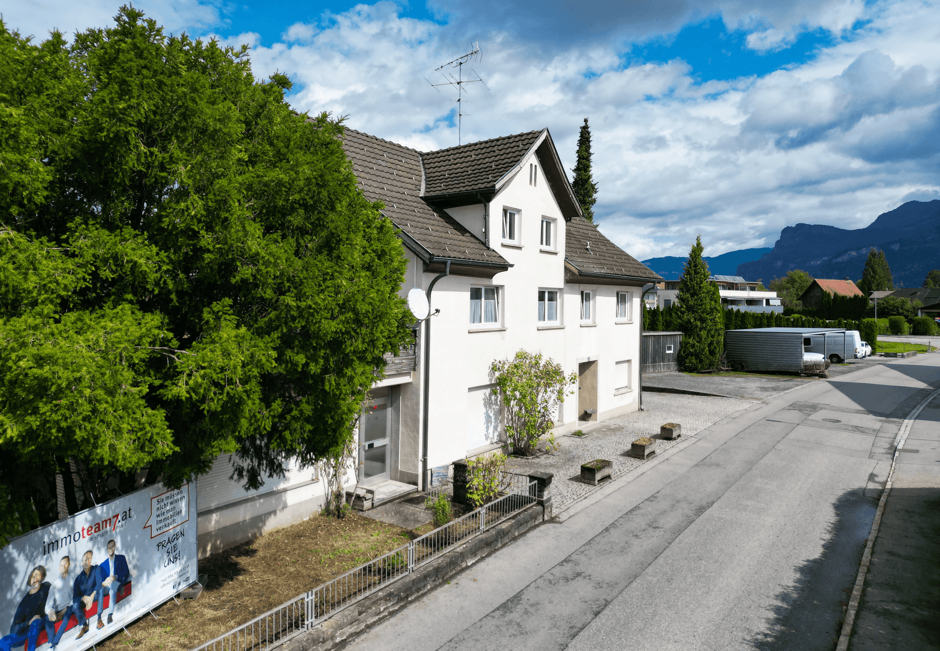 Luftaufnahme des Hauses mit Bergen im Hintergrund und einer Werbetafel im Vordergrund.
