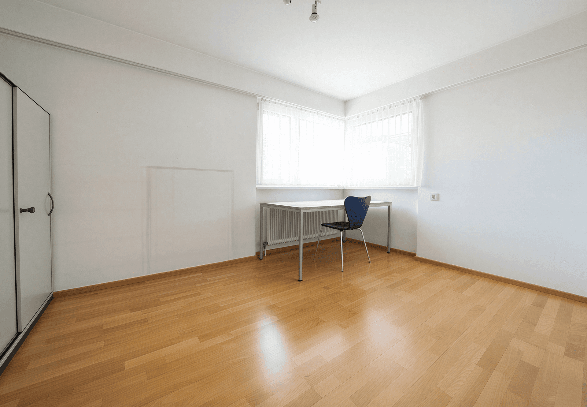 Leeres Zimmer mit hellem Holzboden und großem Fenster, ideal als Schlaf- oder Arbeitszimmer.