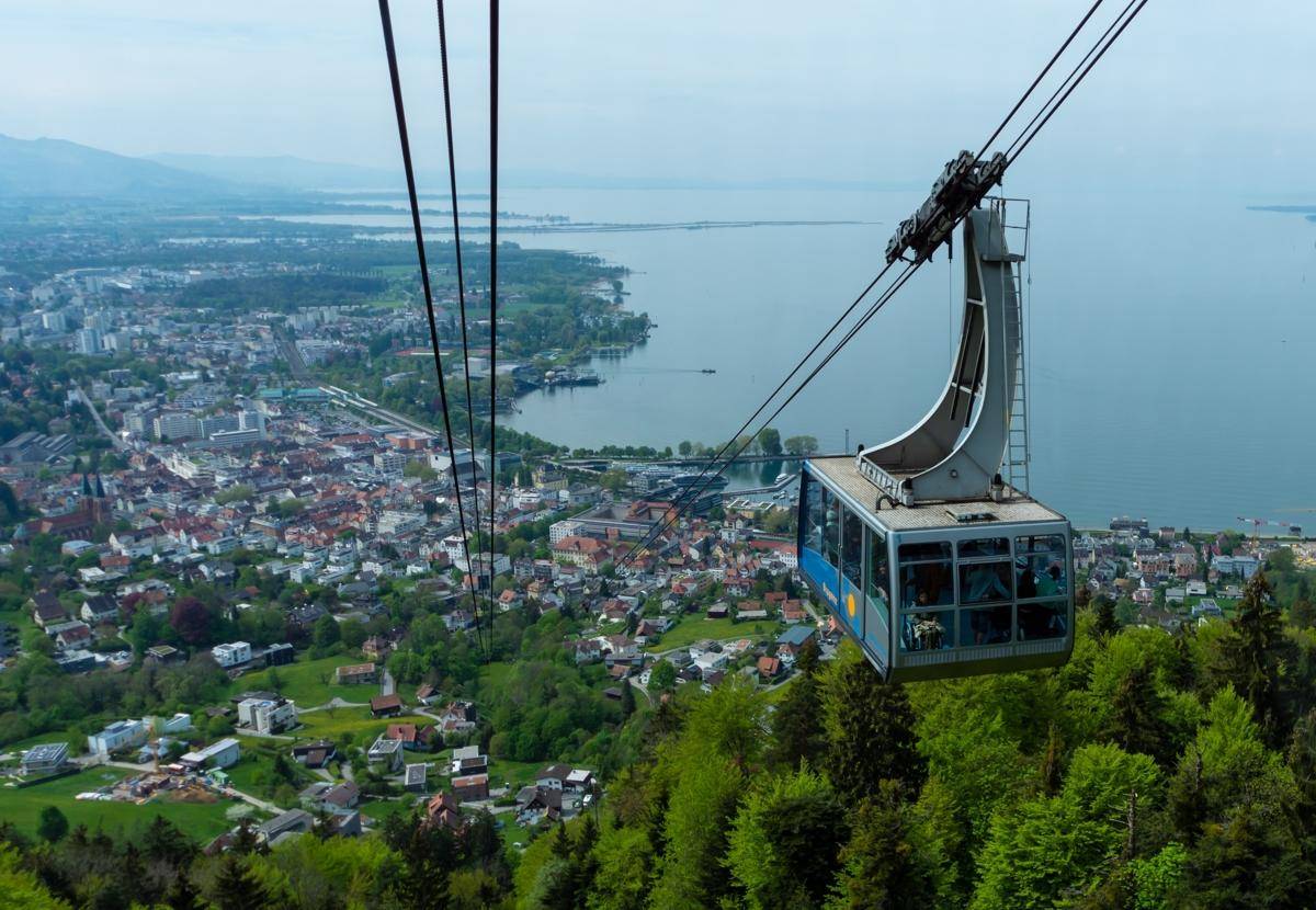 Eine Seilbahn fährt mit Blick auf die Stadt und den Bodensee in der Ferne.