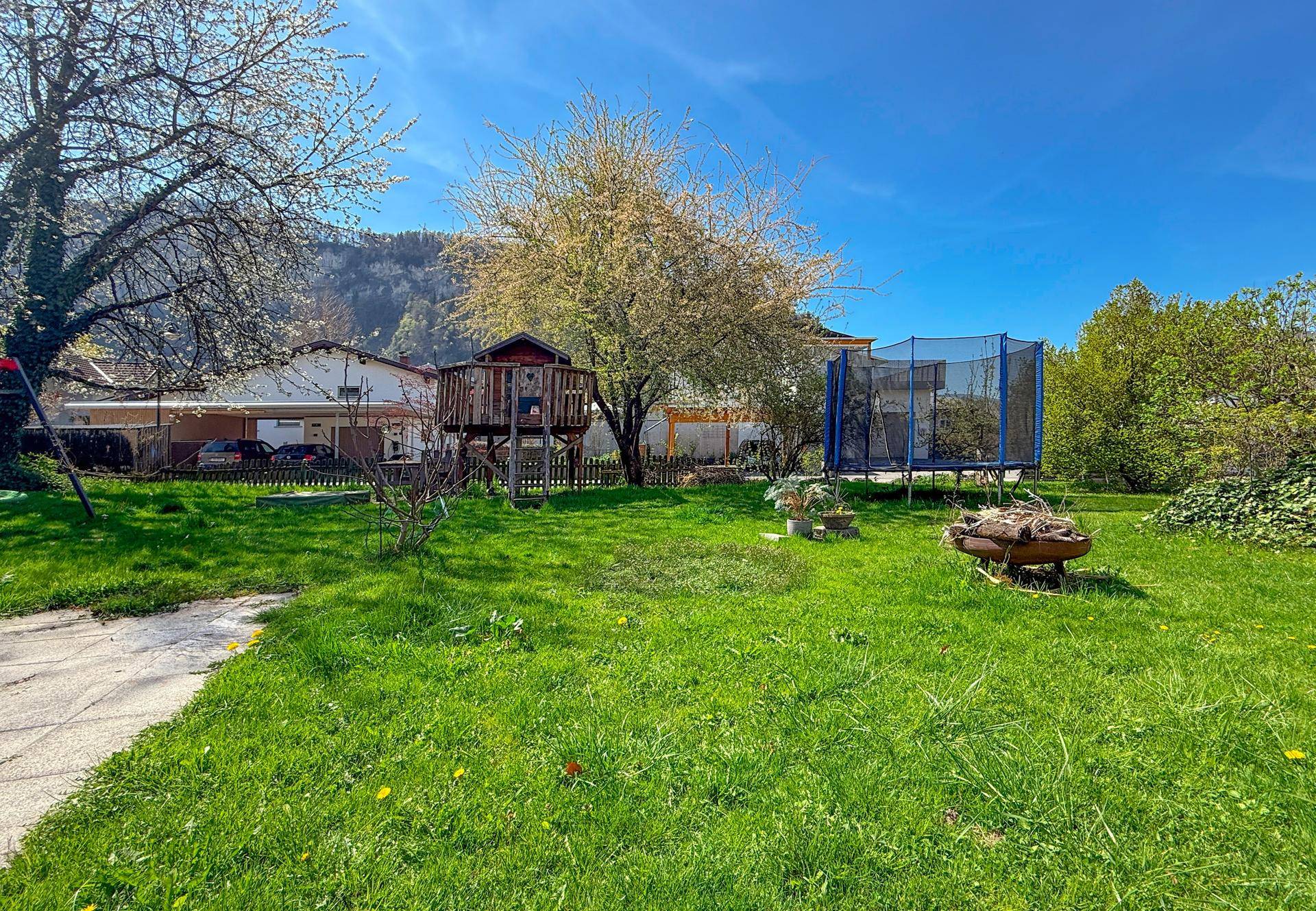 Großer Garten mit Trampolin, Feuerstelle und Blick auf die umliegende Berglandschaft.